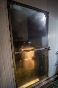 Gas chamber seen through maintenance door - Behind a frosted padlocked door, a hatch can be seen leading into the back of the gas chamber. - Captured at Corowa Slaughterhouse, Redlands NSW Australia.